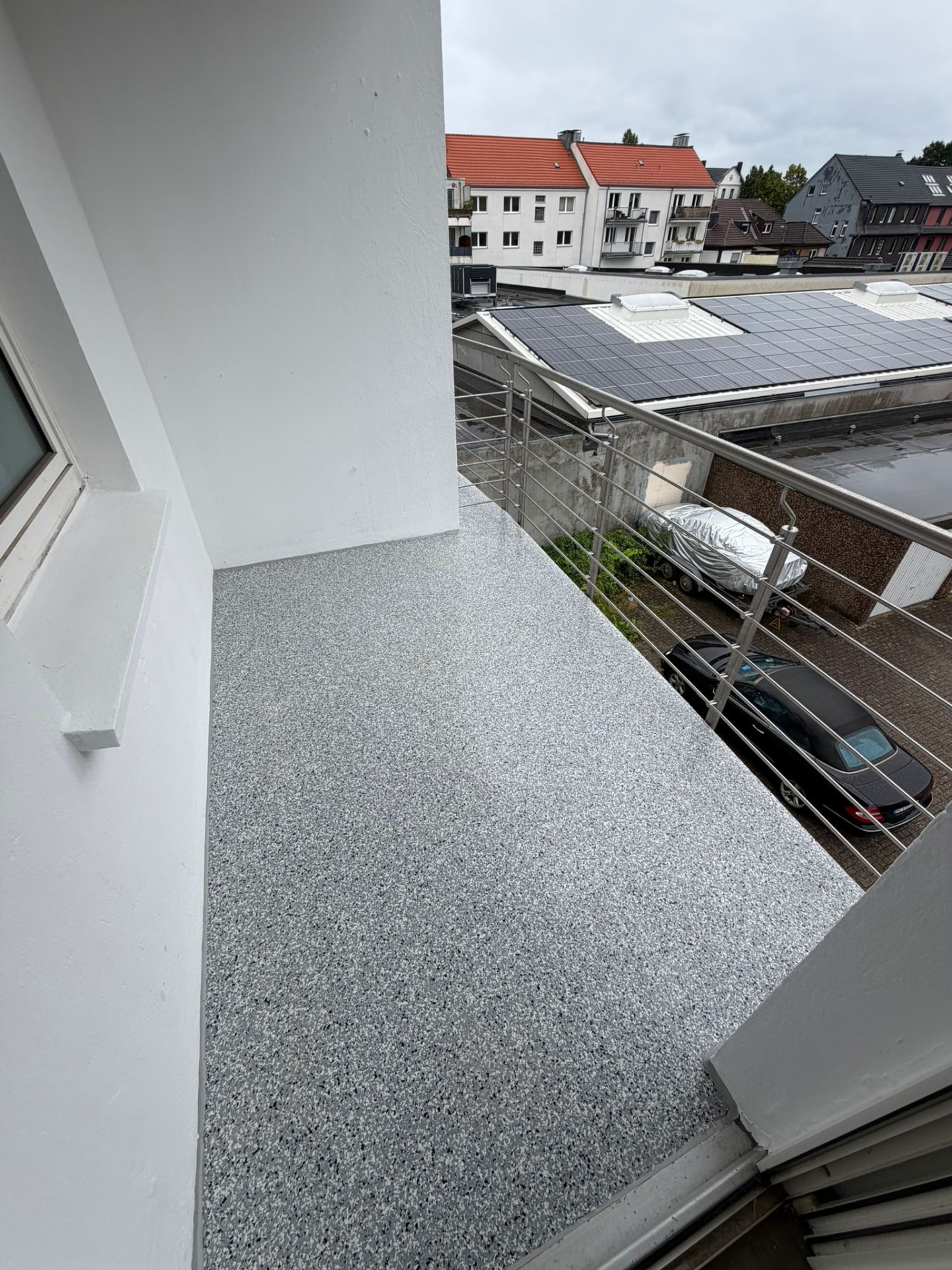 Sanierte Balkonfläche mit grauem Steinteppich und Edelstahlgeländer