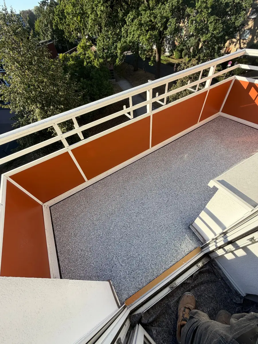 Balkon mit grauem Steinteppich und orangefarbenen Sichtschutzelementen